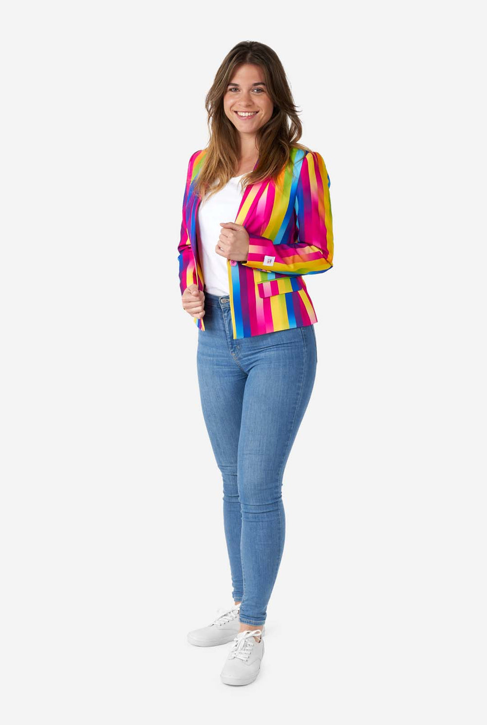 Image of woman wearing vertically striped rainbow colored women's blazer , white shirt and blue jeans. She is holding the sides of the blazer.