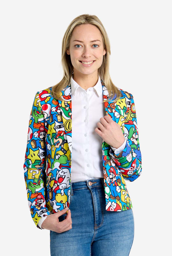 Woman wearing all-over print Super Mario blazer with iconic Super Mario characters. The base is light blue, but there is also yellow, red and white. She is also wearing a jeans and a white blouse.