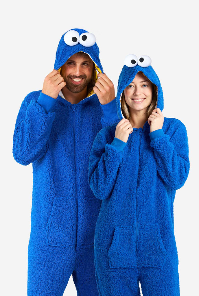 Man and Woman wearing blue pluche Cookie Monster Adult onesie for adults. Standing next to each other, holding hood with hands.