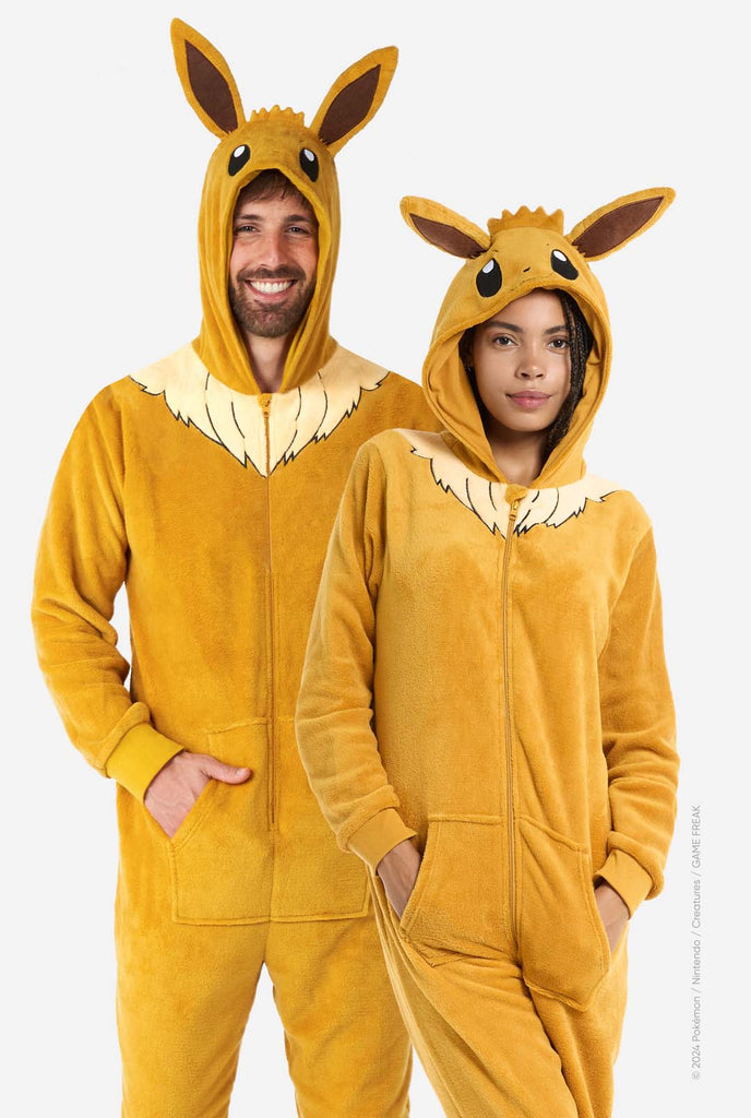 A man and woman are wearing an adorable Eevee onesie, modeled after the beloved Pokémon character. This adult unisex onesie is designed in a warm brown color, resembling Eevee’s fur, and features a fluffy beige collar mimicking Eevee’s mane. The hood includes Eevee's signature large brown ears, big black eyes. The onesie has a front zipper closure and convenient pockets at the front, offering both comfort and ease of wear. Perfect for Pokémon fans.