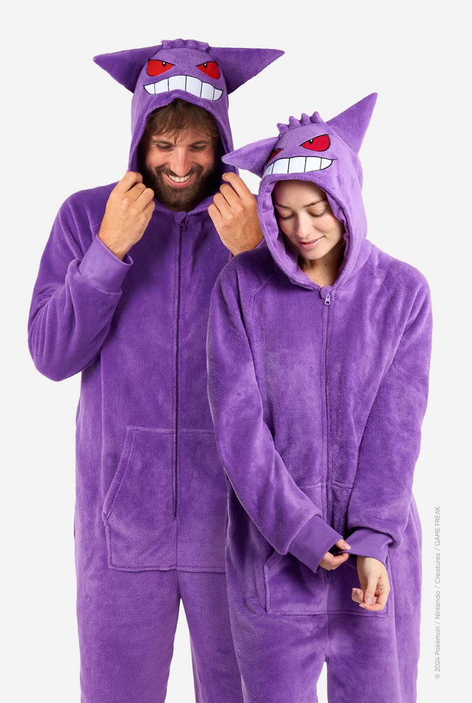 Man and woman wearing purple unisex adult onesie Pokeomon Gengar themed. Both looking at the floor.