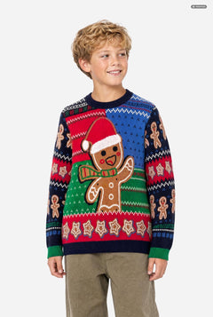 A young boy wearing a festive Christmas knit sweater with a gingerbread man design, paired with khaki pants, photographed against a solid light gray background.