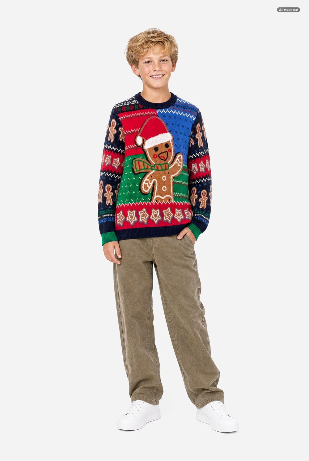 A young boy wearing a festive Christmas knit sweater with a gingerbread man design, paired with khaki pants, photographed against a solid light gray background.