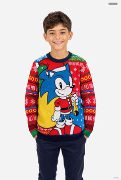 A young boy wearing a festive Christmas knit sweater featuring Sonic the Hedgehog, posed against a solid light gray background.