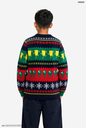 A child viewed from behind wearing a long-sleeve crewneck sweater with a colorful Nordic pattern featuring reindeer, snowflakes, and geometric stripes in green, red, yellow, and navy blue.