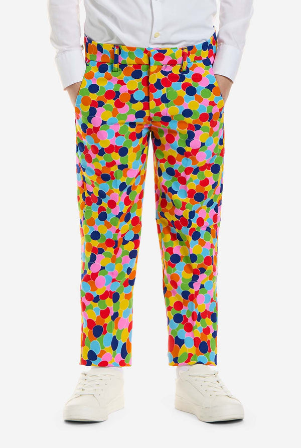In this image, a kid is wearing a boys’ suit with all-over multicolor confetti print and white shirt. The suit has a bright pattern with circles in various colors including orange, yellow, pink, green, blue, and red. Close up of the pants.