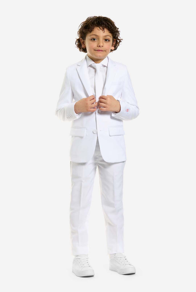 In this image, a kid is wearing a white suit for boys and white shirt. The consists of jacket, pants and clip-on tie. Holding jacket with two hands.