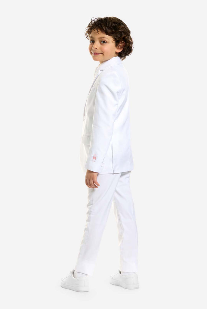 In this image, a kid is wearing a white suit for boys and white shirt. The consists of jacket, pants and clip-on tie. View from the back and head turned to camera.