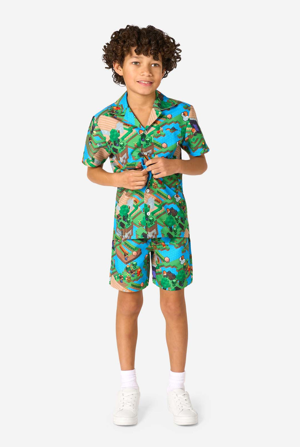 A young boy wearing a colorful summer outfit featuring a Minecraft Overworld print, showcasing pixelated landscapes, characters, and elements from the iconic game. The short-sleeve shirt and matching shorts highlight a vibrant design inspired by the Minecraft universe. 
