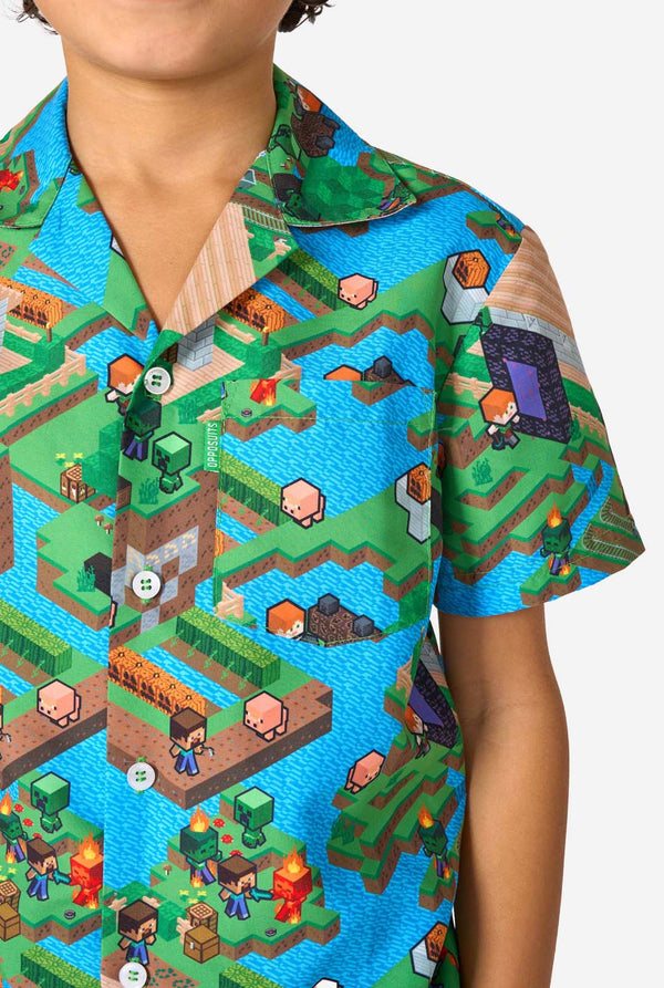 A young boy wearing a colorful summer outfit featuring a Minecraft Overworld print, showcasing pixelated landscapes, characters, and elements from the iconic game. The short-sleeve shirt and matching shorts highlight a vibrant design inspired by the Minecraft universe. Close-up chest.