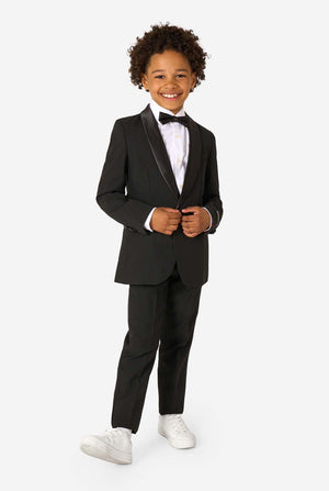 Child wearing a black tuxedo with a white shirt and bow tie on a white background. Full body image.