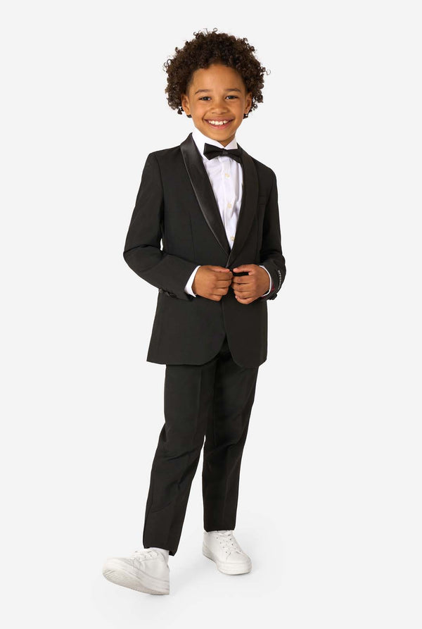 Child wearing a black tuxedo with a white shirt and bow tie on a white background. Full body image.
