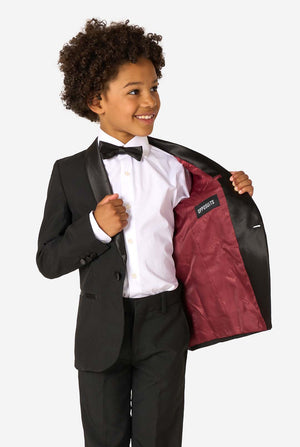 Child wearing a black tuxedo with a red lining, smiling against a white background