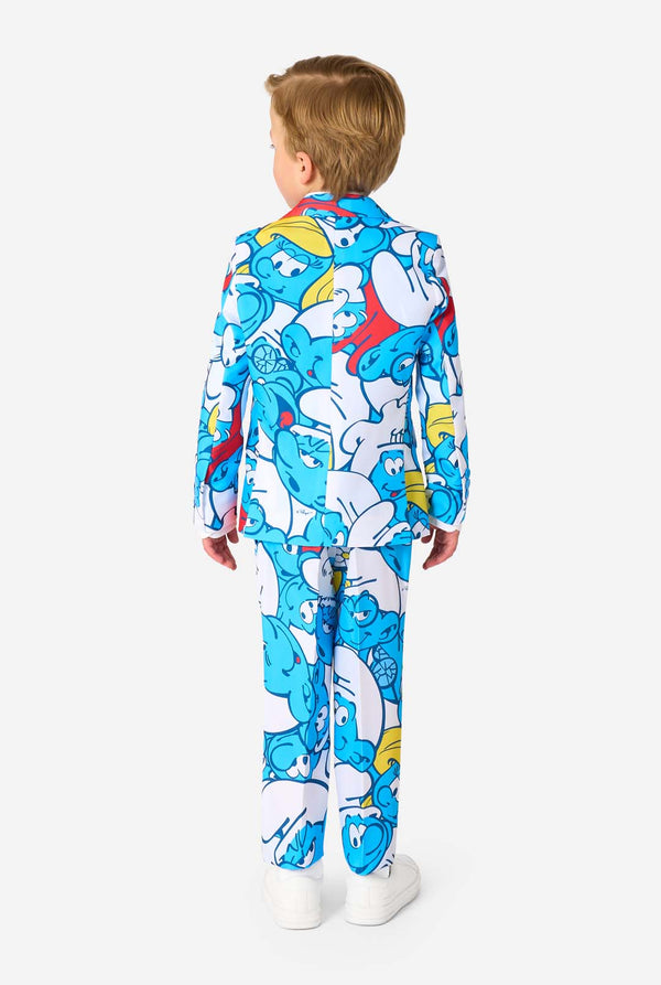 Young boy wearing a colorful Smurfs-themed kids suit featuring vibrant blue cartoon character prints, including jacket, pants, and matching tie, smiling against a plain white background. View from the back.