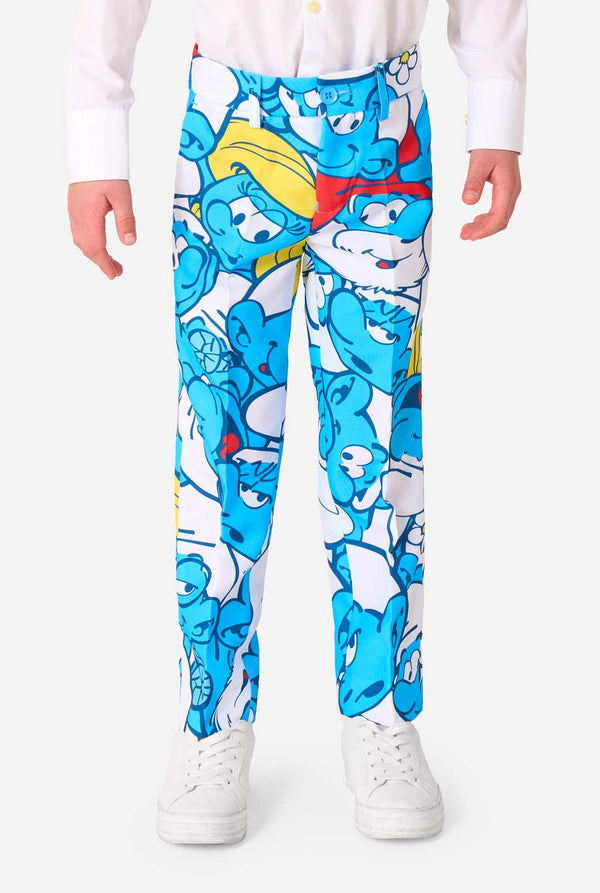 Young boy wearing a colorful Smurfs-themed kids suit featuring vibrant blue cartoon character prints, including jacket, pants, and matching tie, smiling against a plain white background. Pants close-up.