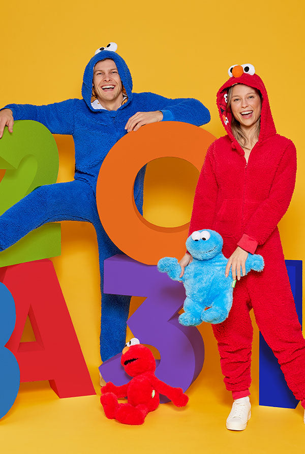 Image of a man and a woman. The man is wearing a Cookie Monster onesie and the woman is wearing a Elmo onesie.