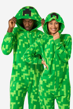 Two people wearing green pixelated Creeper onesies against a white background