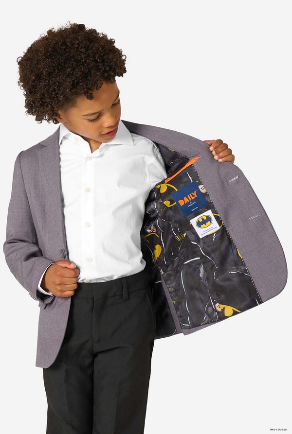 A young boy in a grey blazer looking down, showing the inside lining printed with Batman logos and patterns.