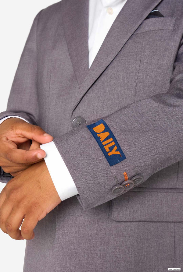 Close-up of the sleeve of a grey blazer with a blue and orange label reading “DAILY.”