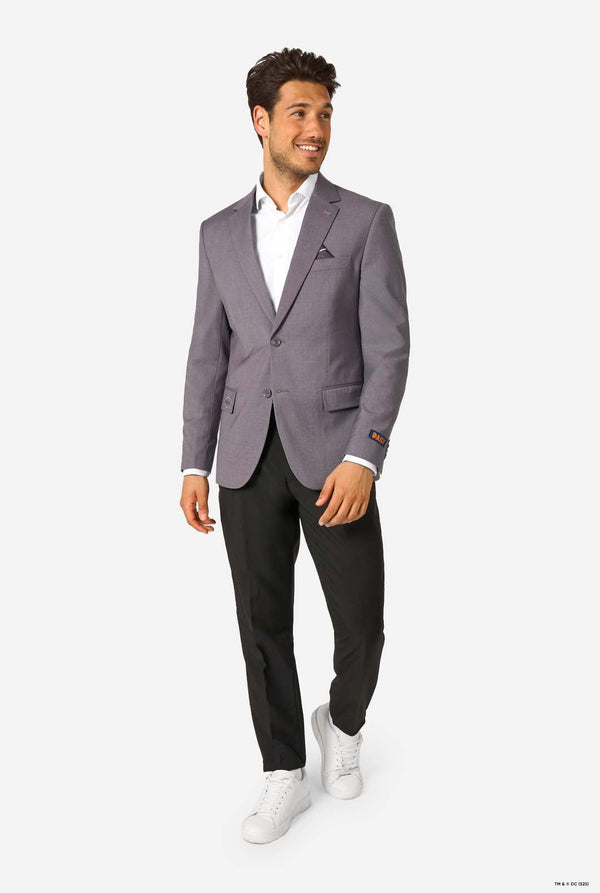 A man wearing a grey blazer, white shirt, black trousers, and white sneakers, smiling while walking.