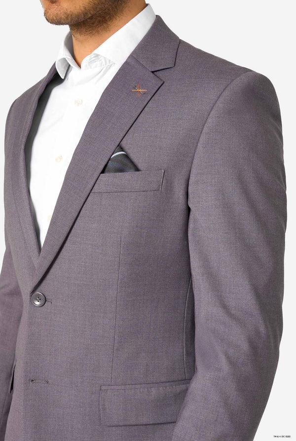 Close-up of the upper part of a grey blazer with a small orange cross-stitch pin and a folded pocket square.