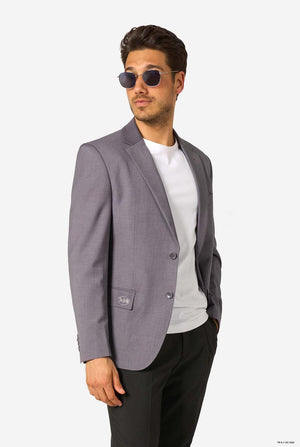 A man wearing a grey blazer, white T-shirt, black trousers, and sunglasses, posing confidently.