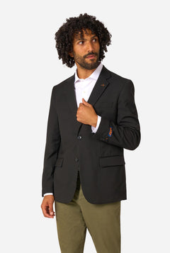 Man wearing a black blazer over a white shirt with green pants on a white background