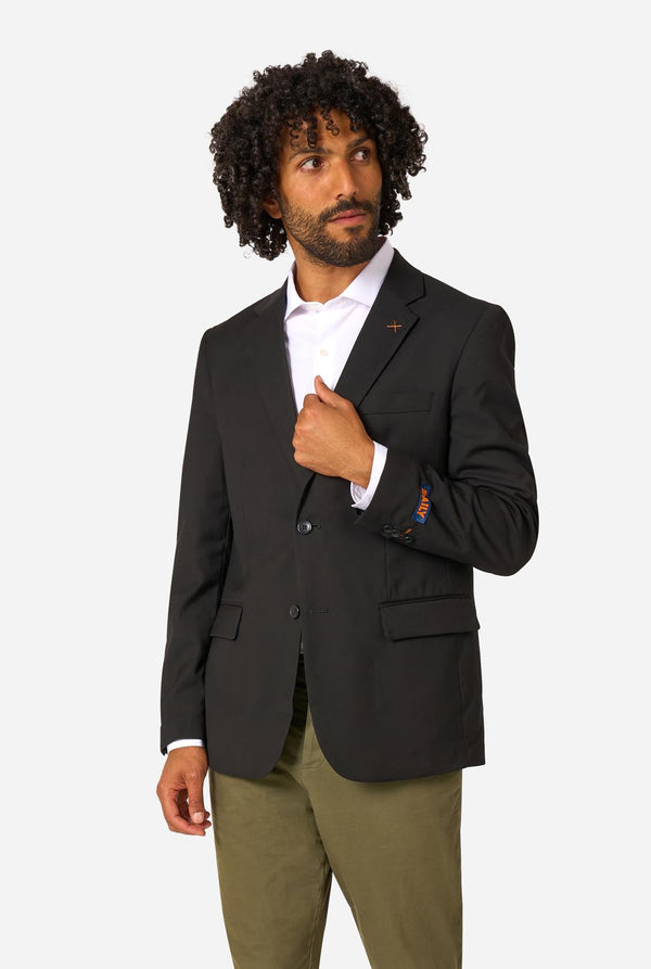 Man wearing a black blazer over a white shirt with green pants on a light background