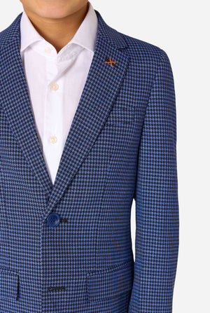 A boy wearing a navy and blue checkered suit with a white dress shirt. The suit has a modern fit with two buttons and flap pockets. He stands against a plain white background. Close up of the chest