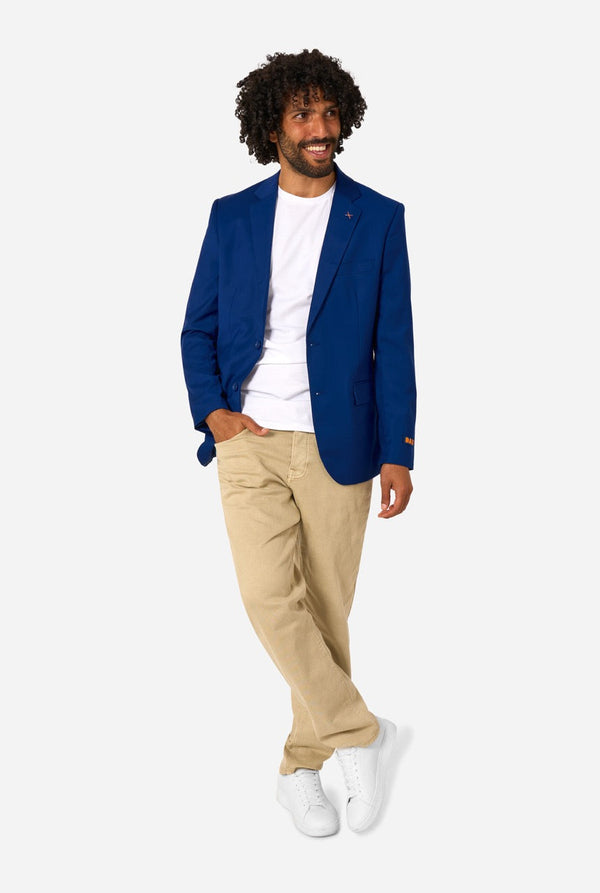 Man wearing a blue blazer, white shirt, beige pants, and white sneakers on a white background