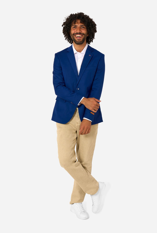 Man wearing a blue blazer, white shirt, beige pants, and white shoes on a white background