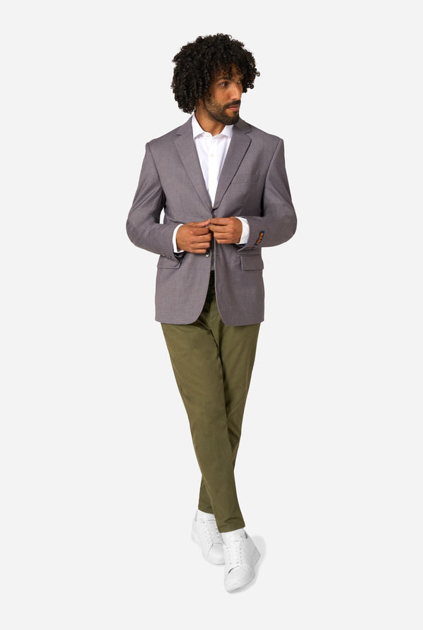 Man wearing a gray blazer, white shirt, green pants, and white shoes on a white background