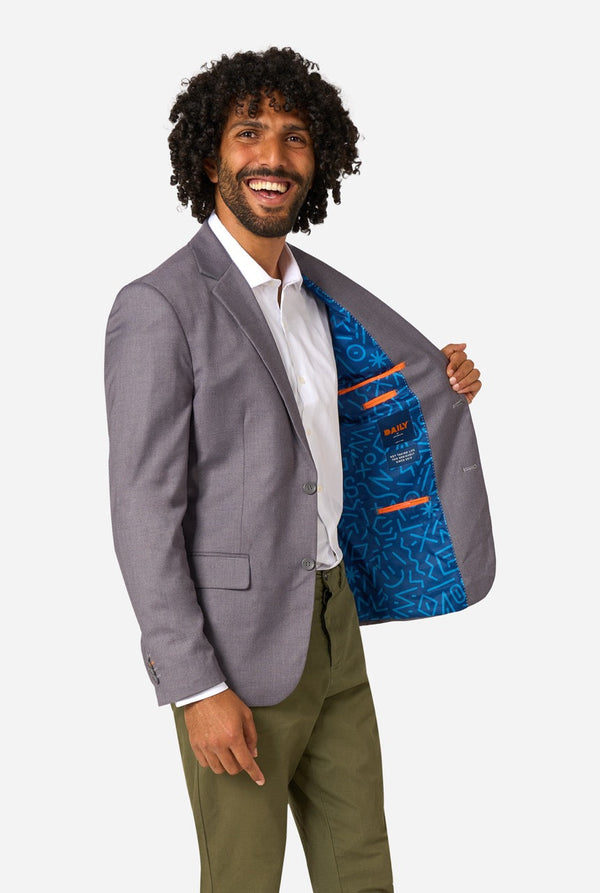 Man wearing a gray blazer with a colorful lining, standing against a white background