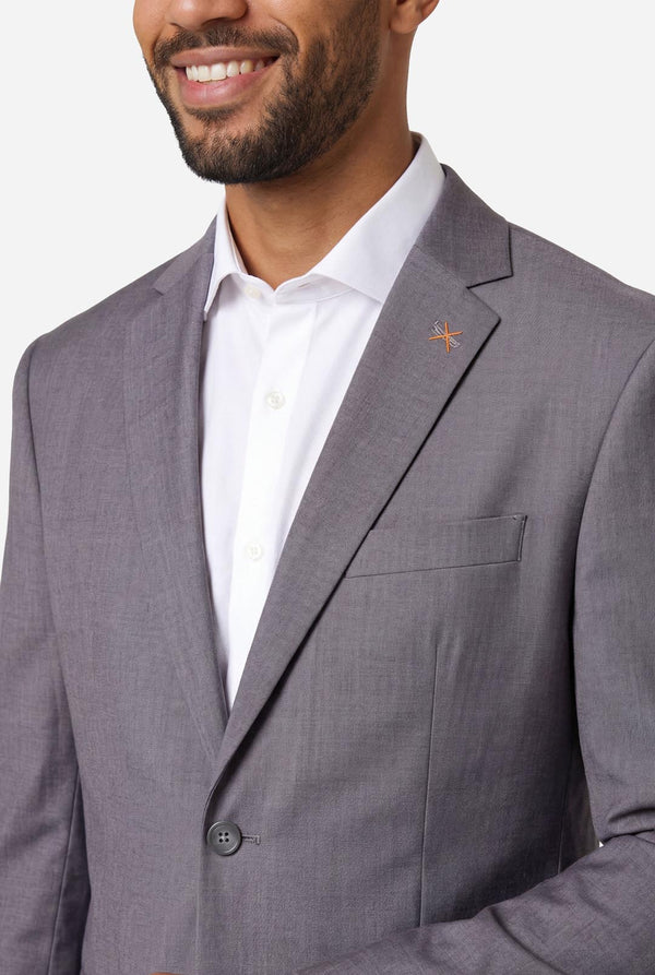 Man wearing a gray suit jacket over a white shirt on a plain background