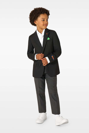 Full-body view of a boy in a black blazer, white shirt, grey trousers, and white sneakers, looking to the side.