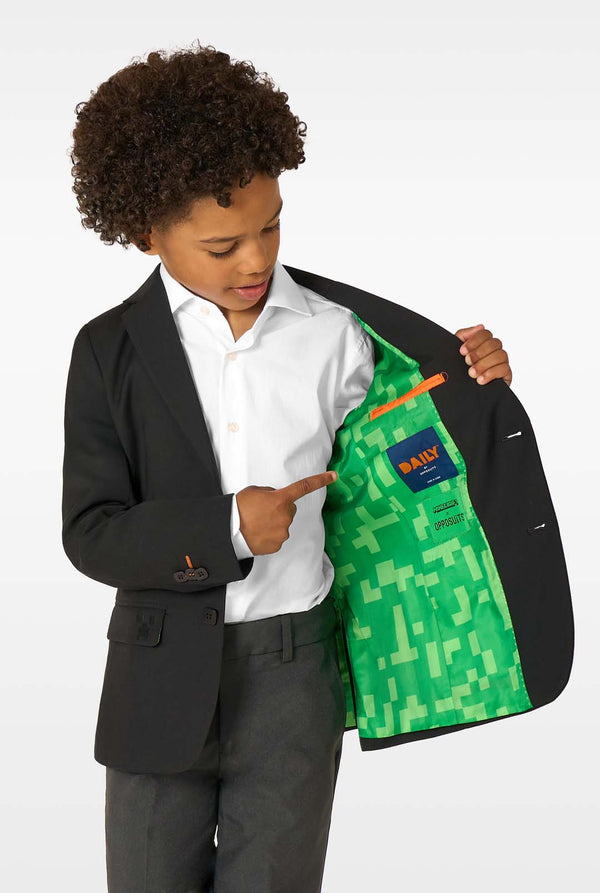 A boy showing the inside of a black blazer lined with green pixel-patterned fabric, pointing at the label.