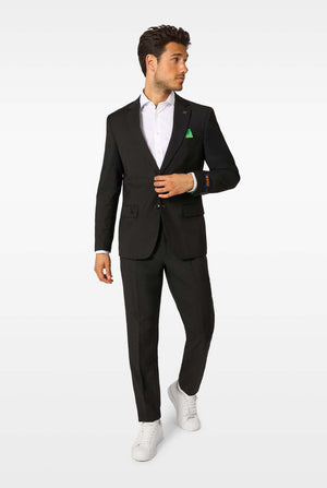 A man wearing a black blazer, white shirt, black trousers, and white sneakers, walking and looking to the side.