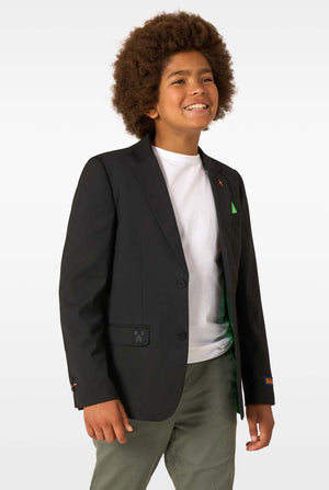A child smiling and walking while wearing a black blazer, white T-shirt, olive trousers, and white sneakers