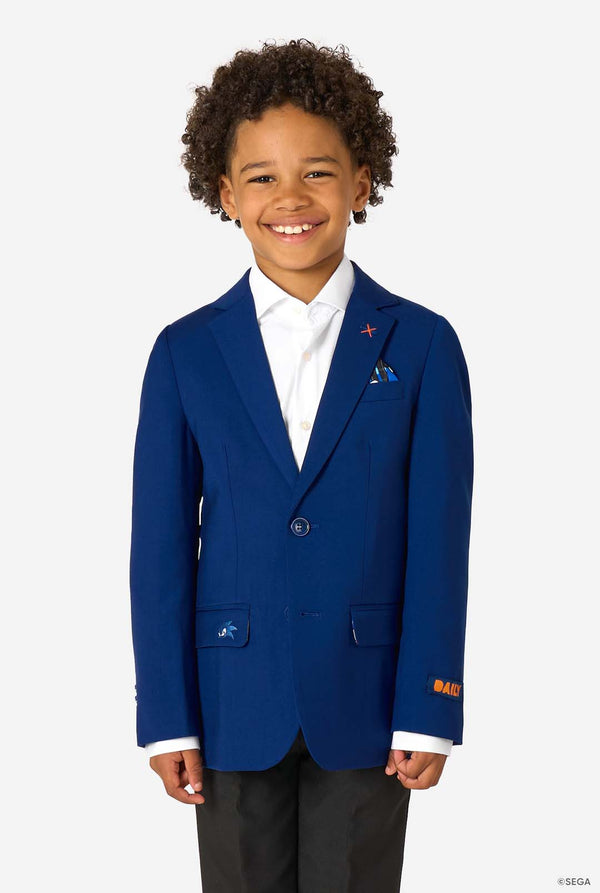 A smiling boy wearing a bright blue blazer, white shirt, and black trousers, standing straight.