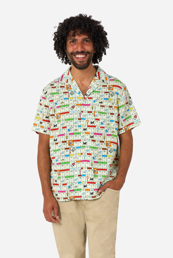 Image of a man wearing a Hawaiian shirt with the Monopoly board in an all-over print on it. He is also wearing a beige pants.