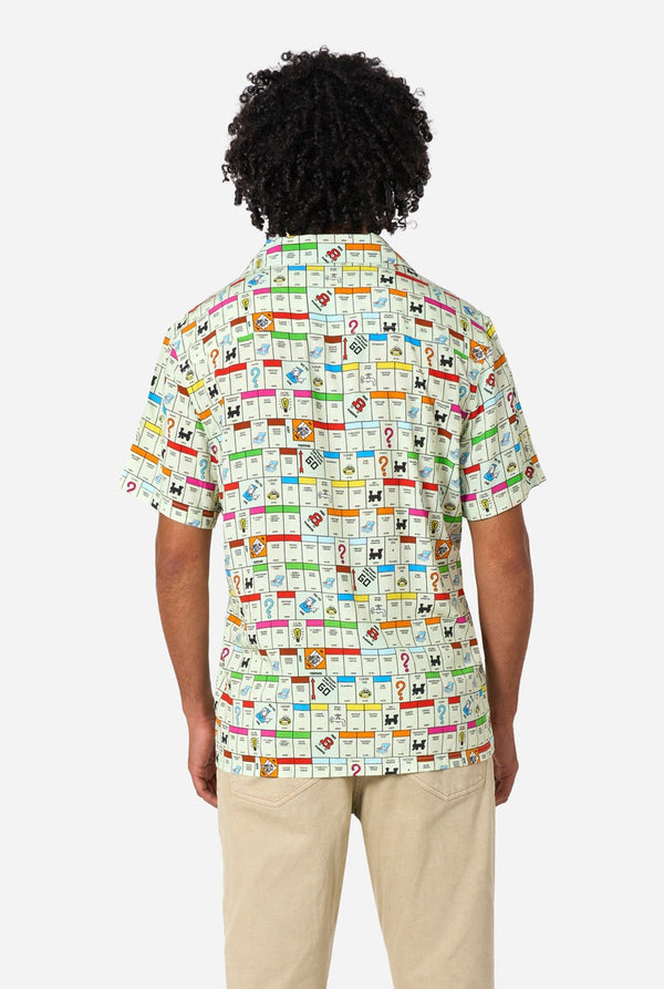 Image of a man wearing a Hawaiian shirt with the Monopoly board in an all-over print on it. He is also wearing a beige pants. View from the back.