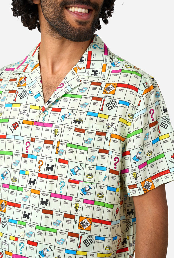 Image of a man wearing a Hawaiian shirt with the Monopoly board in an all-over print on it. Chest close-up.