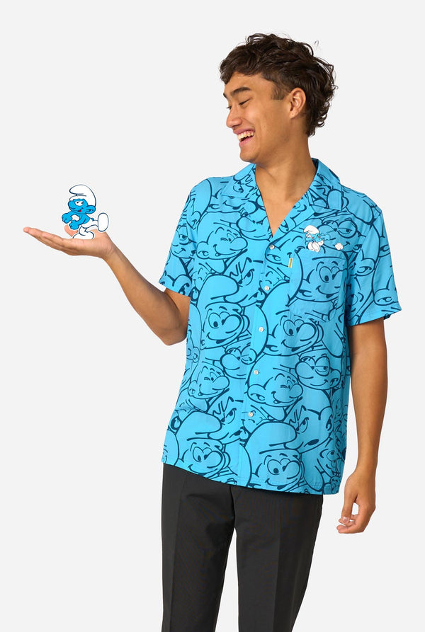 Person wearing a blue Smurf pattern shirt holding a small Smurf figure against a white background