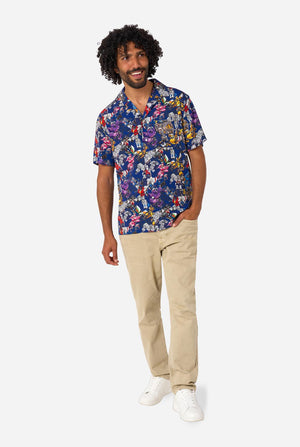 Man wearing a colorful patterned Transformer shirt on a light background. Full body image.