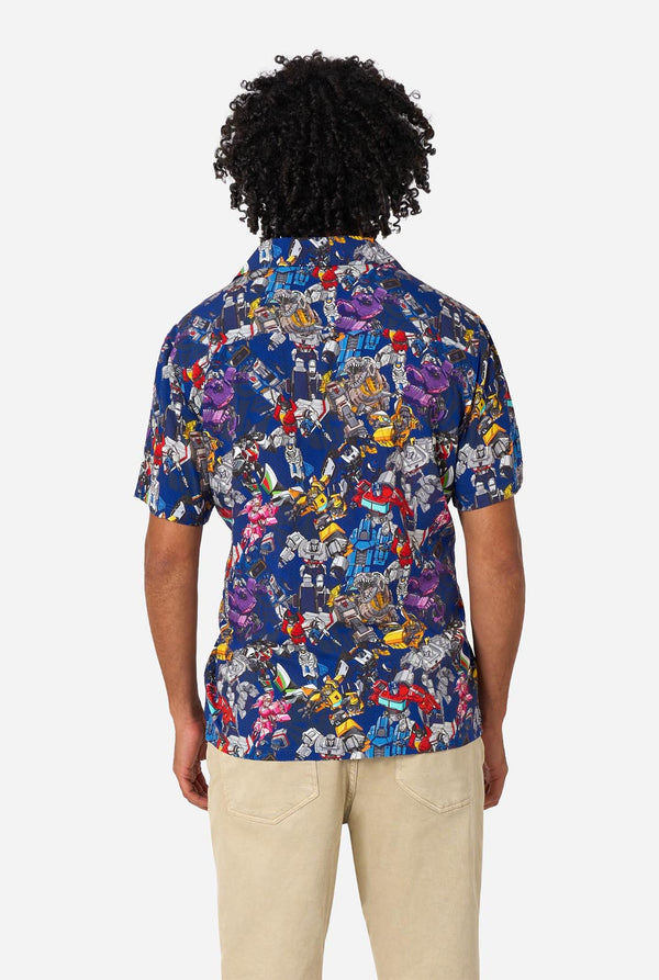 Man wearing a colorful patterned Transformer shirt on a light background. View from the back.