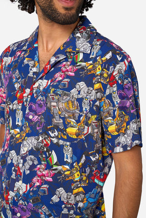 Man wearing a colorful patterned Transformer shirt on a light background. Chest close-up.