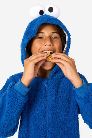 A kid is wearing a blue sesame street onesie resembling Cookie Monster. Kid eating cookies.