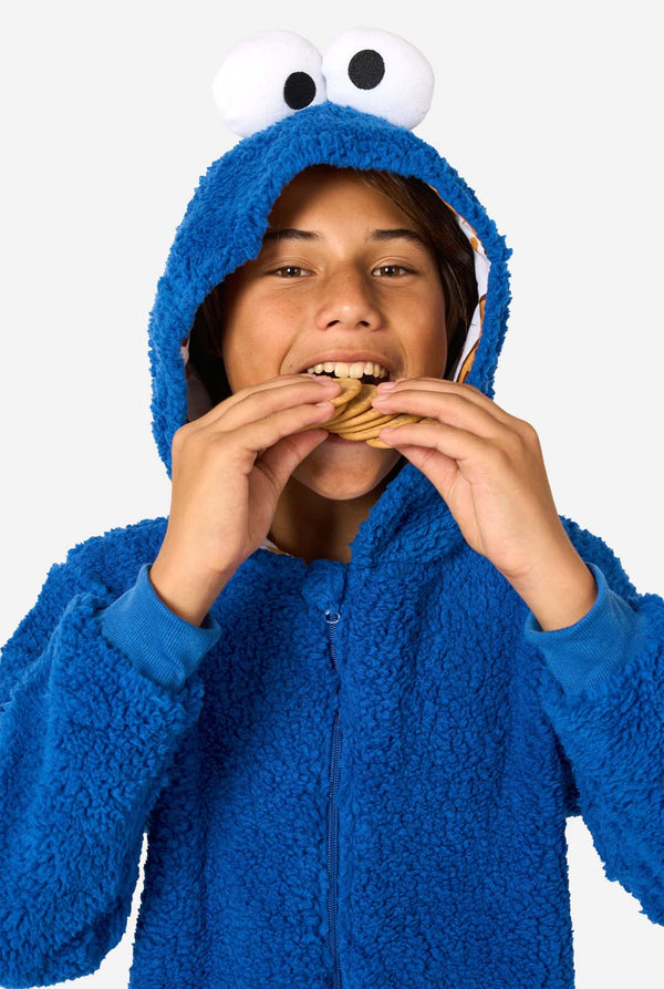 A kid is wearing a blue sesame street onesie resembling Cookie Monster. Kid eating cookies.