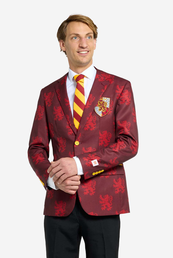 Image with light grey background and man wearing Harry Potter suit, Gryffindor styled. Suit consists of red blazer with Gryffindor logo and light red lions all over print, black pants, and red and yellow diagonal striped tie.     