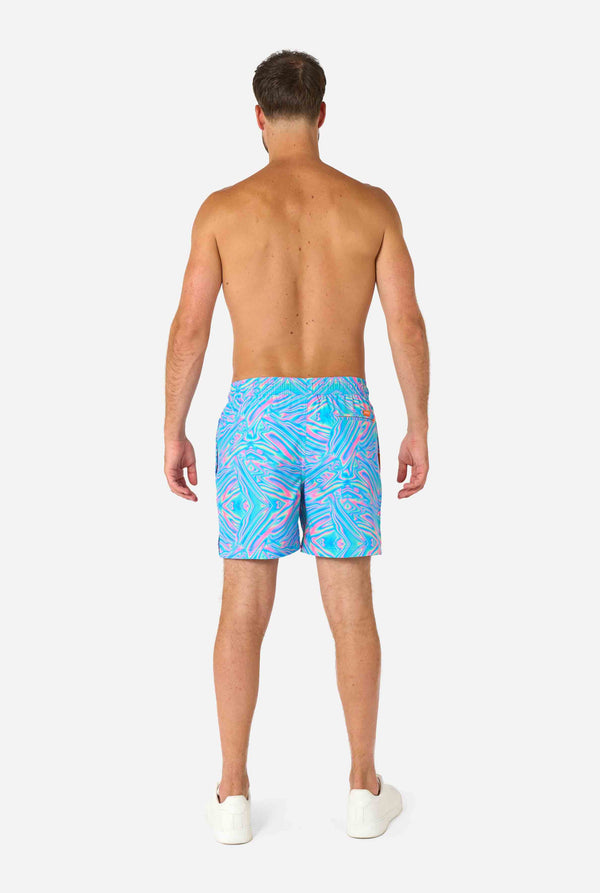 Man wearing a men's vibrant holographic swim shorts with a mesmerizing blue, pink, and purple swirl design. Eye-catching and stylish swimwear for summer fun. View from the back.
